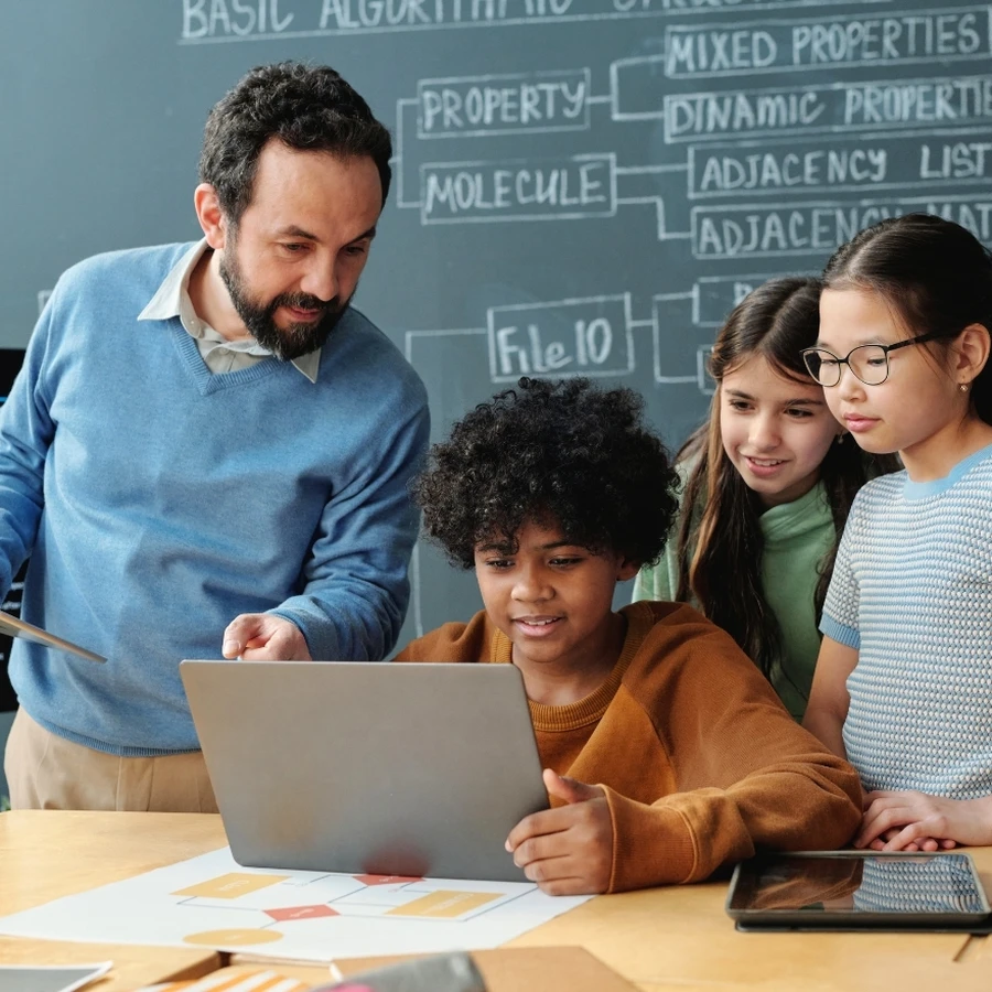 Teacher and students collaborating on a laptop in a classroom