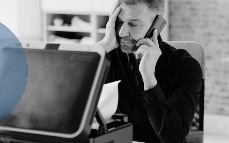 A man on the phone in front of a faulty printer 