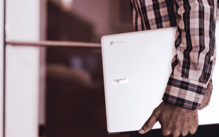 Person walking into a building while holding a Chromebook