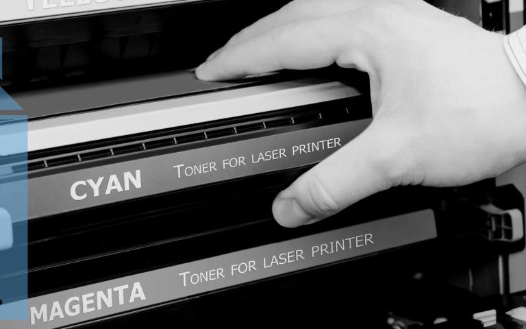 A person grabbing a toner cartridge from a laser printer