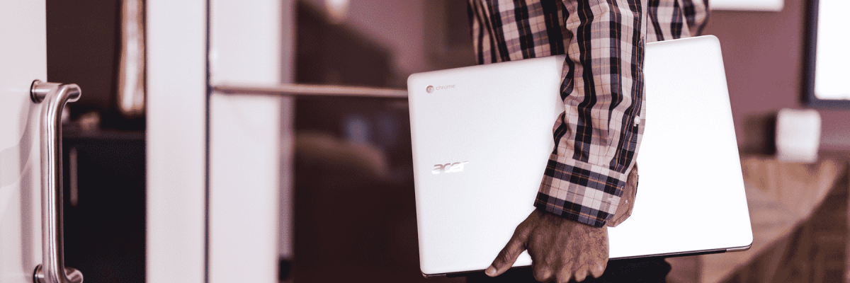 Person walking into a building while holding a Chromebook