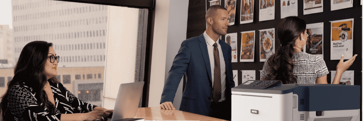 Three people working in an office next to the Xerox C310 printer