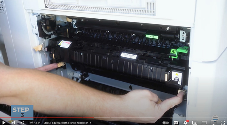 Printer technician squeezes orange handles on bottom of fuser of Xerox AltaLink printer