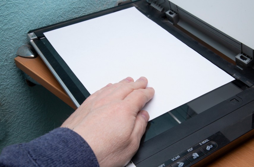 A closeup of a person's hand positioning a paper on a printer's platen glass to scan