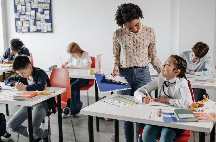 A teacher handing a student a notebook in a classroom